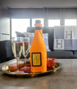 A bottle of champagen on a tbale with a Hermes throw in the back ground. 