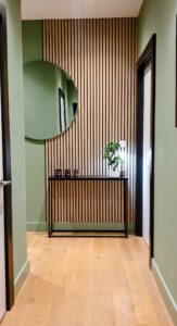 The image show a small space after being designed to create a big impact upon entering the property. Natural green walls accent black door frames and an eyecatching focal display.